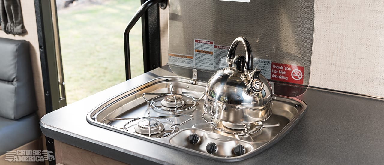 three burner stove top range in open position with tea kettle.